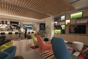 Un bar moderno con barra, asientos y sillas de colores, un televisor y una planta.