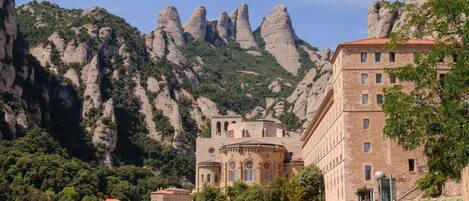 A historic building with a prominent dome and arched windows, surrounded by lush greenery and rocky mountains.