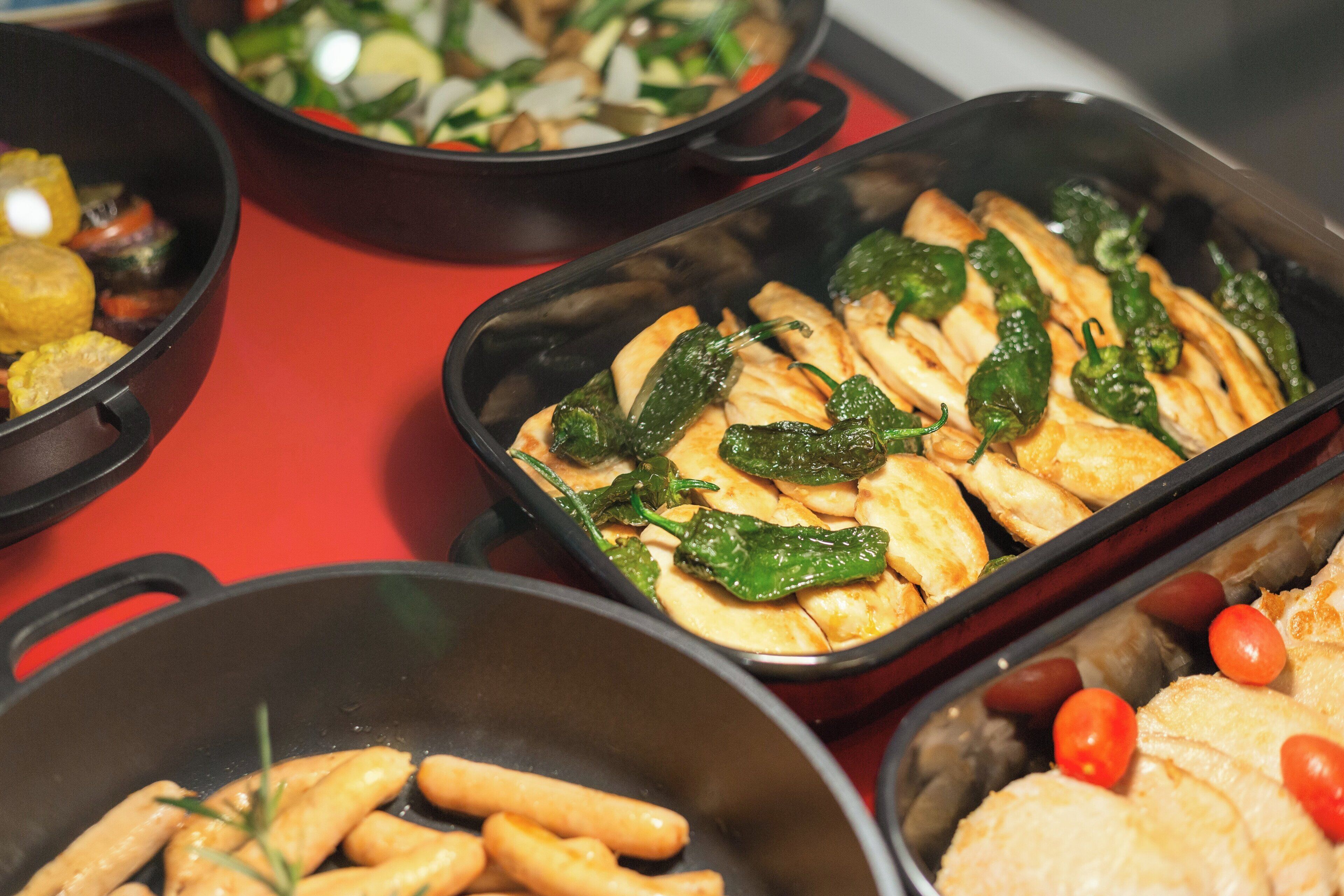 A variety of dishes in black serving dishes on a red table.