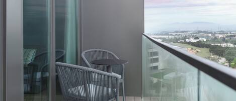 A balcony with wicker chairs and a table, overlooking a cityscape with buildings and a bridge.