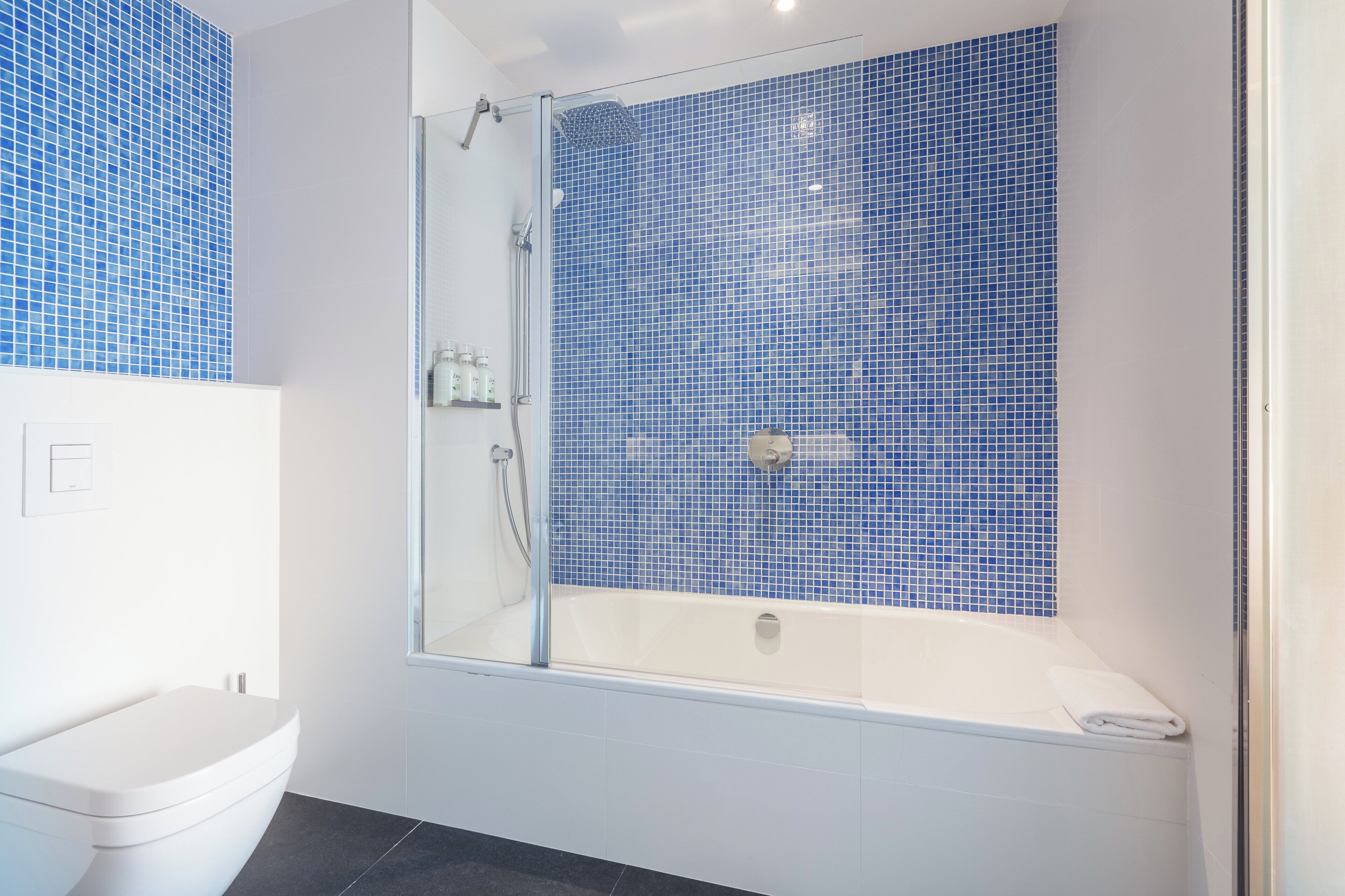 Un baño moderno con ducha envuelta en vidrio, una bañera blanca y azulejos de mosaico azul en las paredes.