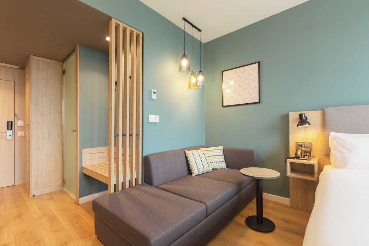 Une chambre d’hôtel moderne avec un canapé, une petite table ronde, une table de chevet avec une lampe et un lit.