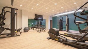 Een sportschool met diverse fitnessapparaten, waaronder loopbanden, krachttoestellen en een roeimachine.