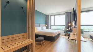 Een moderne hotelkamer met een bed, een bureau, een stoel, een bankje en een groot raam met uitzicht.