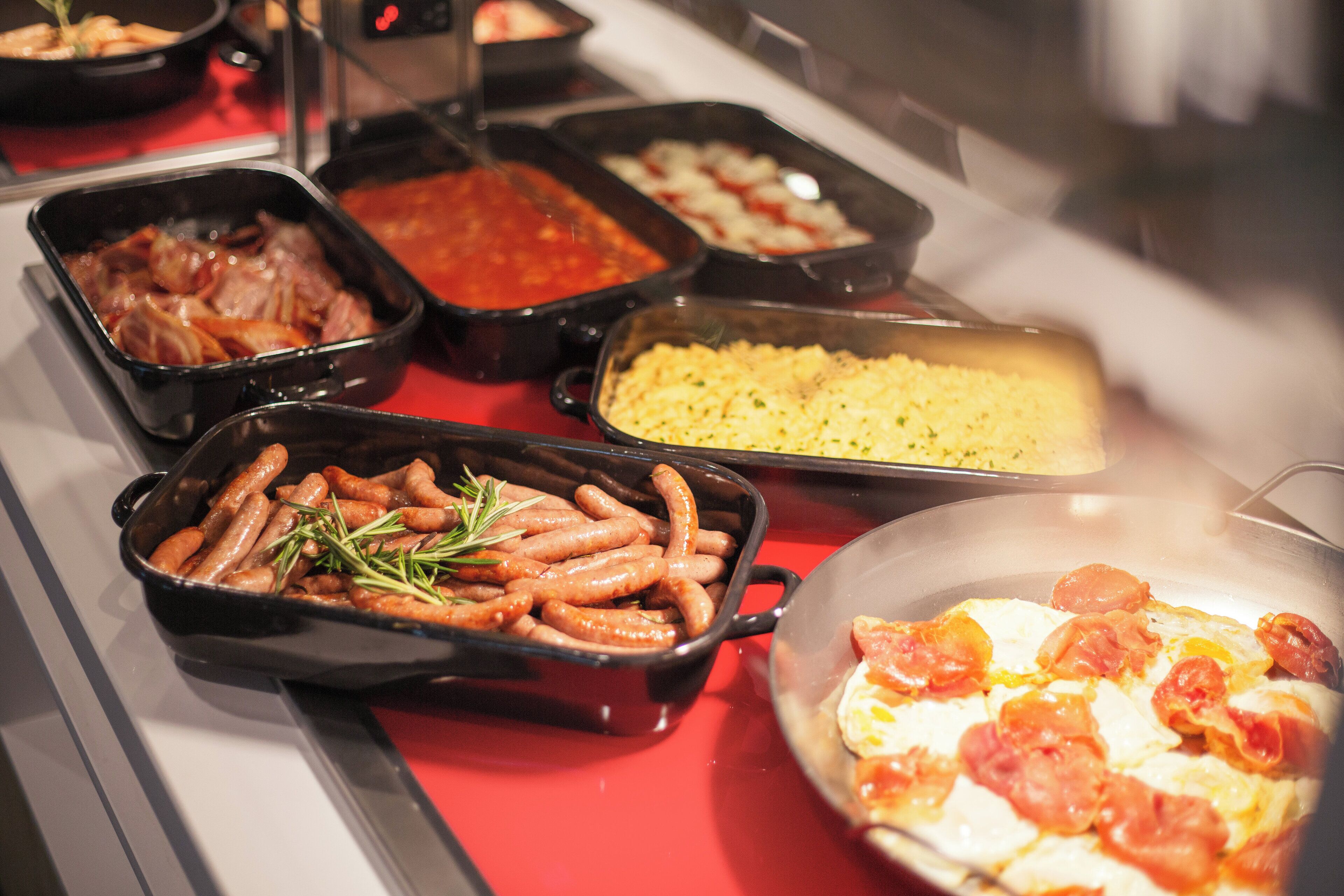 Un bufé con diversos platos, incluyendo salchichas, pasta y un pastel de carne.