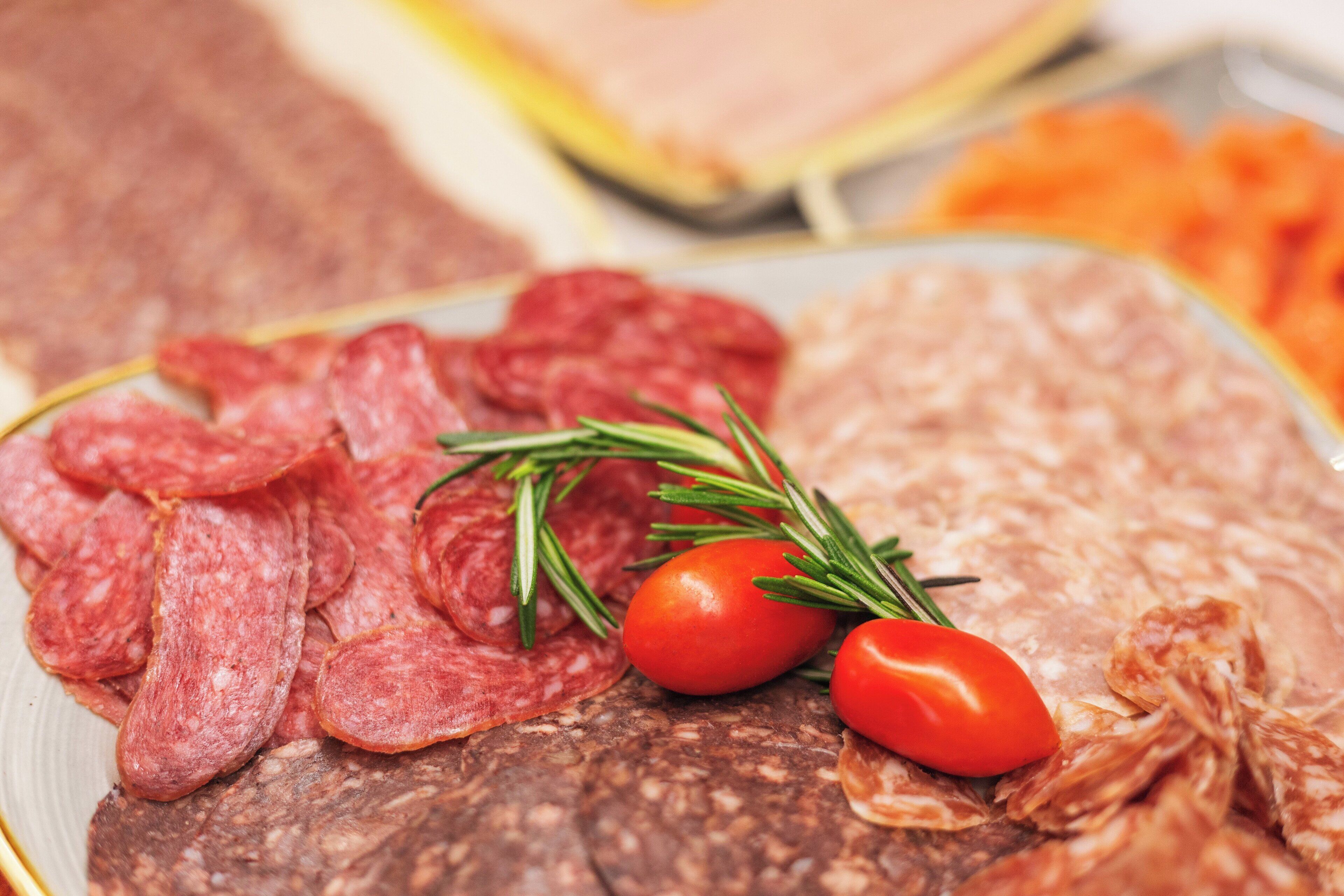 A variety of sliced meats, including salami and prosciutto, arranged on a plate with rosemary and cherry tomatoes.