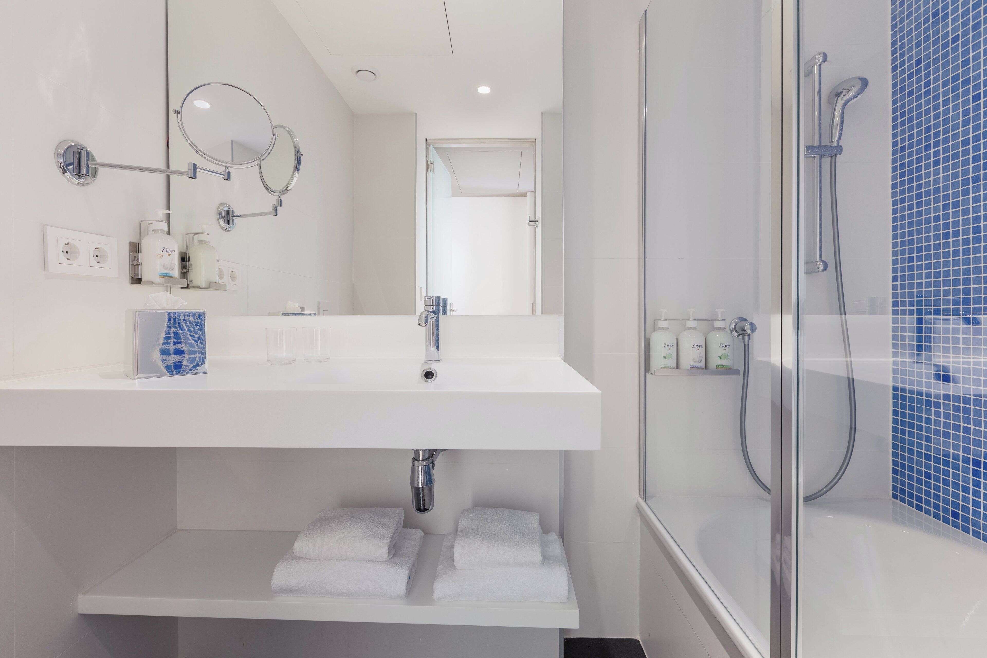 A modern bathroom with a white sink, a mirror, a handheld showerhead, and a glass-enclosed shower.