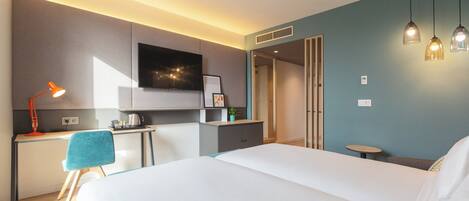 A modern hotel room with a large bed, a desk with a chair, a flat-screen TV, and a small table with a lamp.