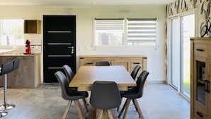 Une cuisine moderne avec un coin repas, comprenant une grande table en bois, des chaises noires et une porte noire.