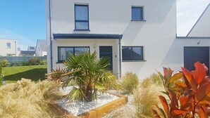 Une maison moderne à deux étages, avec une façade blanche, une porte d’entrée et deux fenêtres à l’étage supérieur.