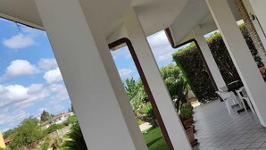 Un espacio al aire libre cubierto con suelo de baldosas, pilares blancos y plantas en macetas.