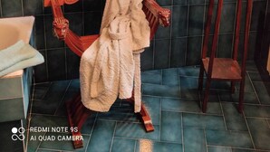 Un baño con pared de baldosas a cuadros, una silla de madera con una toalla, un taburete de madera pequeño y un florero en la pared.