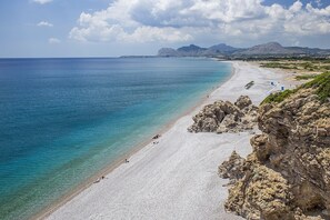 Ein Küstenstrand mit felsigen Klippen, klarem türkisblauem Wasser und einer ausgedehnten Sandküste.