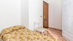 Ein kleines Zimmer mit einem Bett, einem Sessel, einem Kleiderschrank und einer Tür.