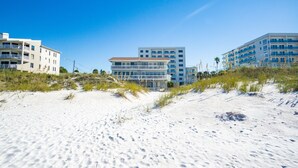 Un hotel frente a la playa con varios pisos, techo plano y una playa arenosa en primer plano.