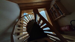 Una escalera en espiral de madera con vistas a una habitación que tiene una estantería y una ventana.