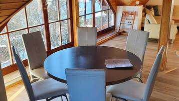 Ein geräumiges Zimmer mit hoher Decke und großen Fenstern, ausgestattet mit einem runden Tisch und Stühlen, mit Blick ins Freie.