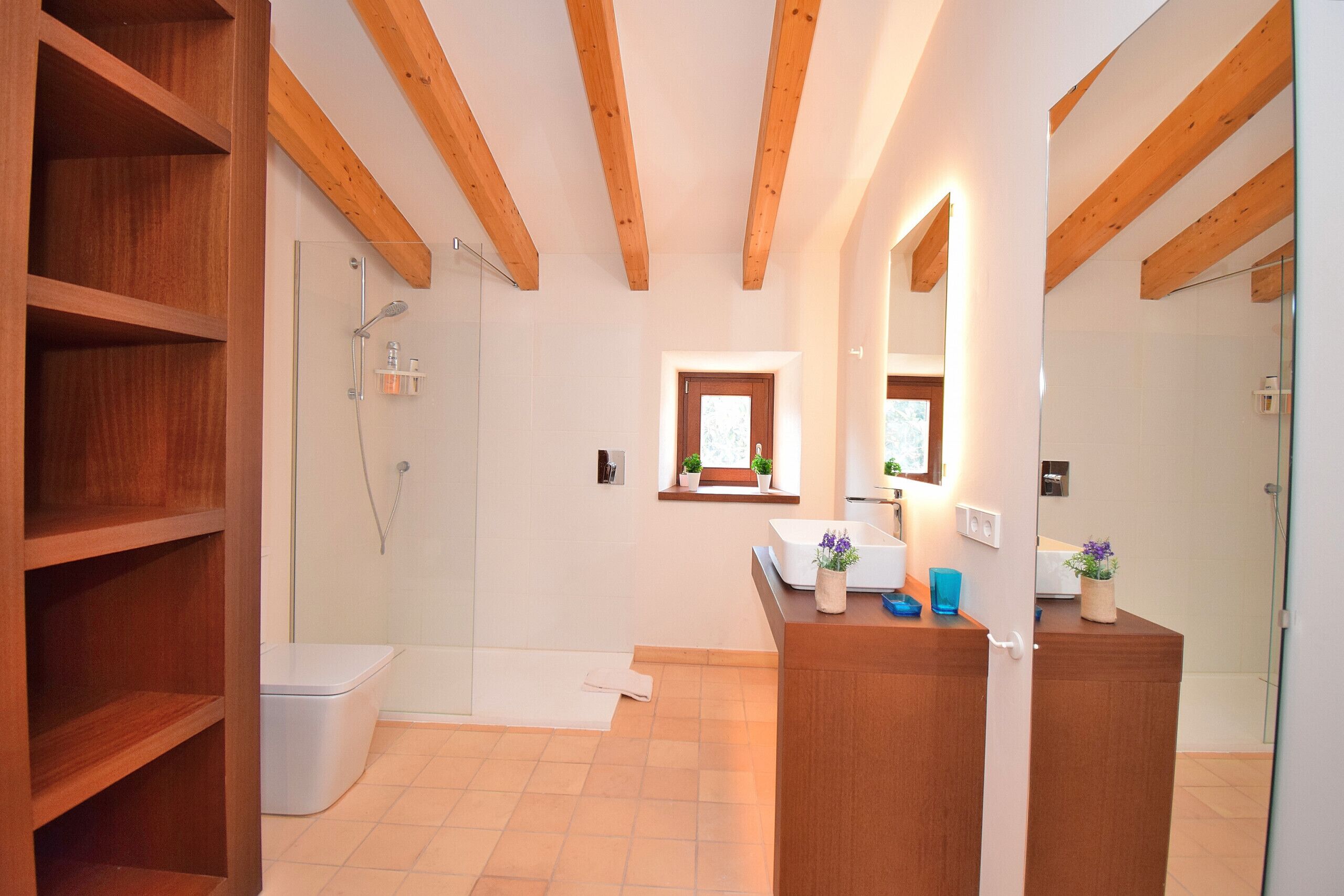 A modern bathroom with wooden beams, a glass shower enclosure, a toilet, and a vanity with a mirror.