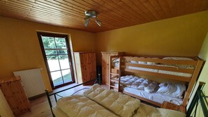 Ein Zimmer mit einem Etagenbett, Holzboden, Heizkörper und einem Fenster mit Blick auf Grünflächen.