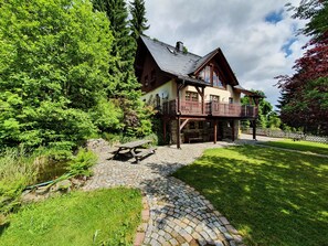 A chalet-style house with a stone patio, wooden deck, and a picnic table.