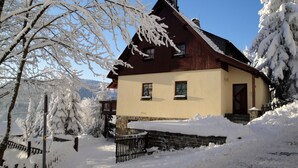 Ein schneebedecktes Haus mit Holzfassade und Steinunterbau.