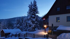 Eine verschneite Landschaft mit einem Haus, einem Holzzaun und einem mit Schnee bedeckten Baum.
