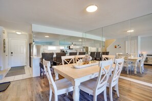 Uma cozinha moderna com armários brancos, uma ilha central e um espaço de refeições com cadeiras brancas e uma mesa de madeira.