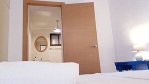 Ein Hotelzimmer mit Holztür, einem Bett mit weißer Bettdecke, einem Nachttisch mit Lampe und einem Spiegel an der Wand.