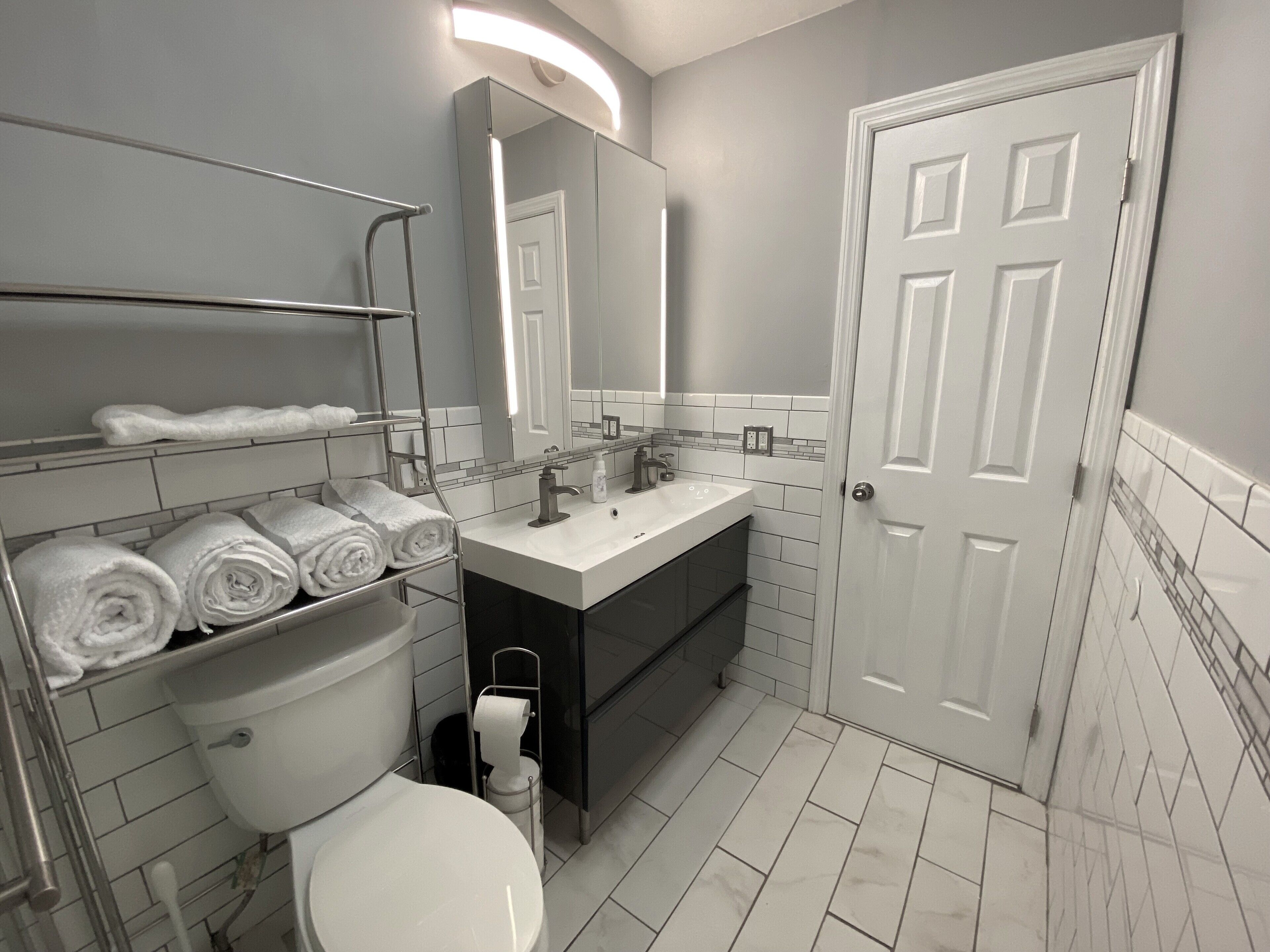 Een moderne badkamer met toilet, wastafel en spiegel. Er zijn planken met handdoeken en een toiletrolhouder.
