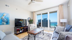 A living room with a flat-screen TV, a sofa, a coffee table, and a balcony with a view of the city and the sea. - Ariel Dunes I 1407 *Beach Access*3 pools* (Miramar Beach)