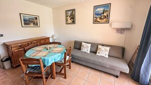 A dining area with a wooden table and chairs, a sofa, and two wall-mounted paintings. - L'Amirauté by Interhome (Bormes-les-Mimosas)