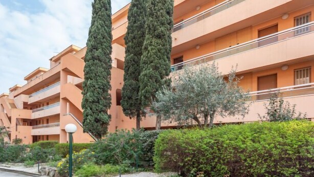 A multi-story residential building with balconies, surrounded by greenery and tall cypress trees. - L'Amirauté by Interhome (Bormes-les-Mimosas)