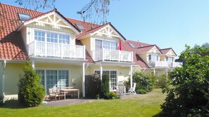 Houses with white balconies and red-tiled roofs, each featuring a front porch with outdoor furniture.