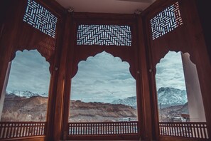 Una habitación con tres ventanas de madera con elaborados diseños de celosía, que ofrece vistas a montañas nevadas y un valle.