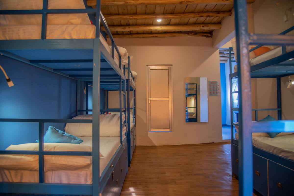 A dormitory room with bunk beds, wooden floors, a door, and a small window.