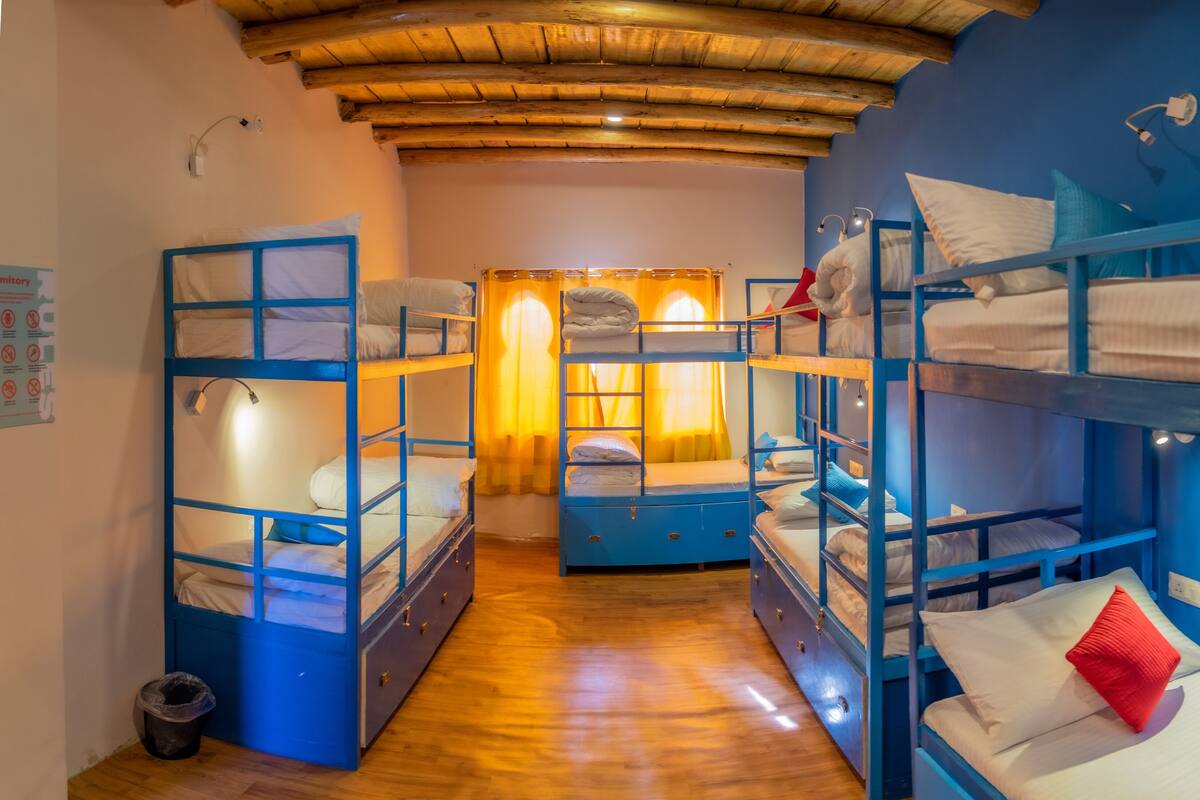 A dormitory room with bunk beds, wooden floors, and a wooden ceiling.