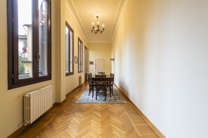 Un couloir doté d’un plancher en bois, une table à manger avec des chaises et un lustre.