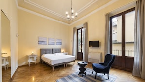A hotel room with a large bed, a chair, a small table, a chandelier, and a TV on the wall. - Duomo Luxury House by Mmega (Florence)