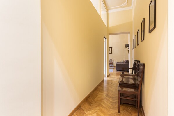A hallway with wooden flooring, a bench, and framed pictures on the wall.