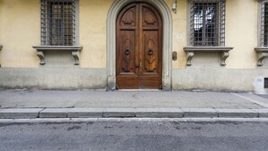 A double wooden door with a decorative arch above it, flanked by two windows with metal bars. - Duomo Luxury House by Mmega (Florence)