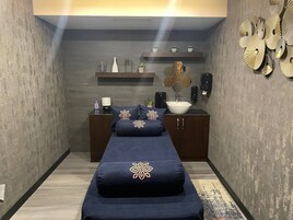 A narrow room with a bed, a small table with a vase, and a wall with decorative items.