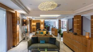 A modern hotel lobby with a reception desk, seating area, and a large chandelier.