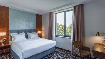 Habitación de hotel con una cama grande, una silla, un escritorio y un ventanal con cortinas.
