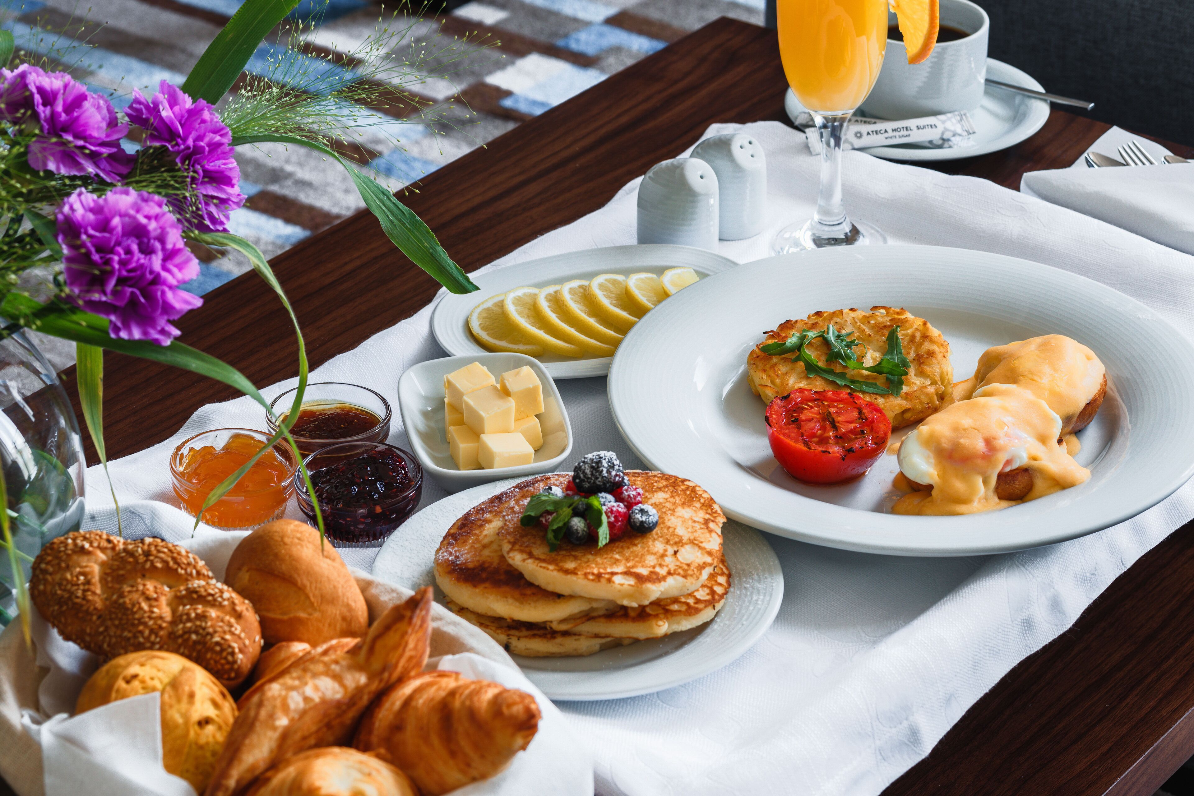 A breakfast table with croissants, pancakes, and a fruit salad.