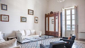Un salón moderno con un sofá blanco, una mesa de centro de cristal, un espejo grande y vistas al mar a través de una puerta abierta.