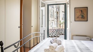 Una habitación de hotel con una cama, vistas a un patio con tejados de tejas y un cuadro en la pared.