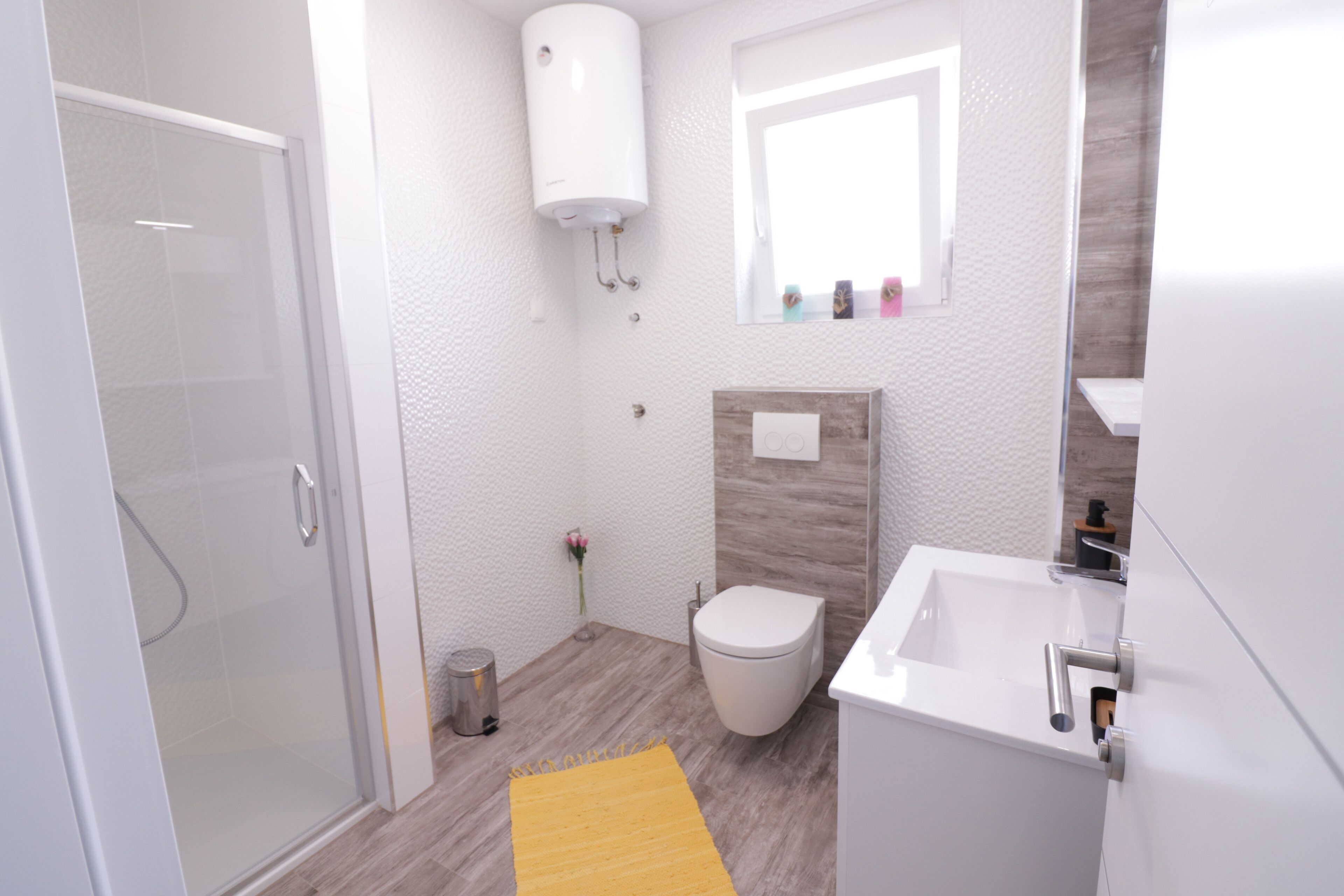 A modern bathroom with a glass shower enclosure, a toilet, a sink, and a white heater mounted on the wall.
