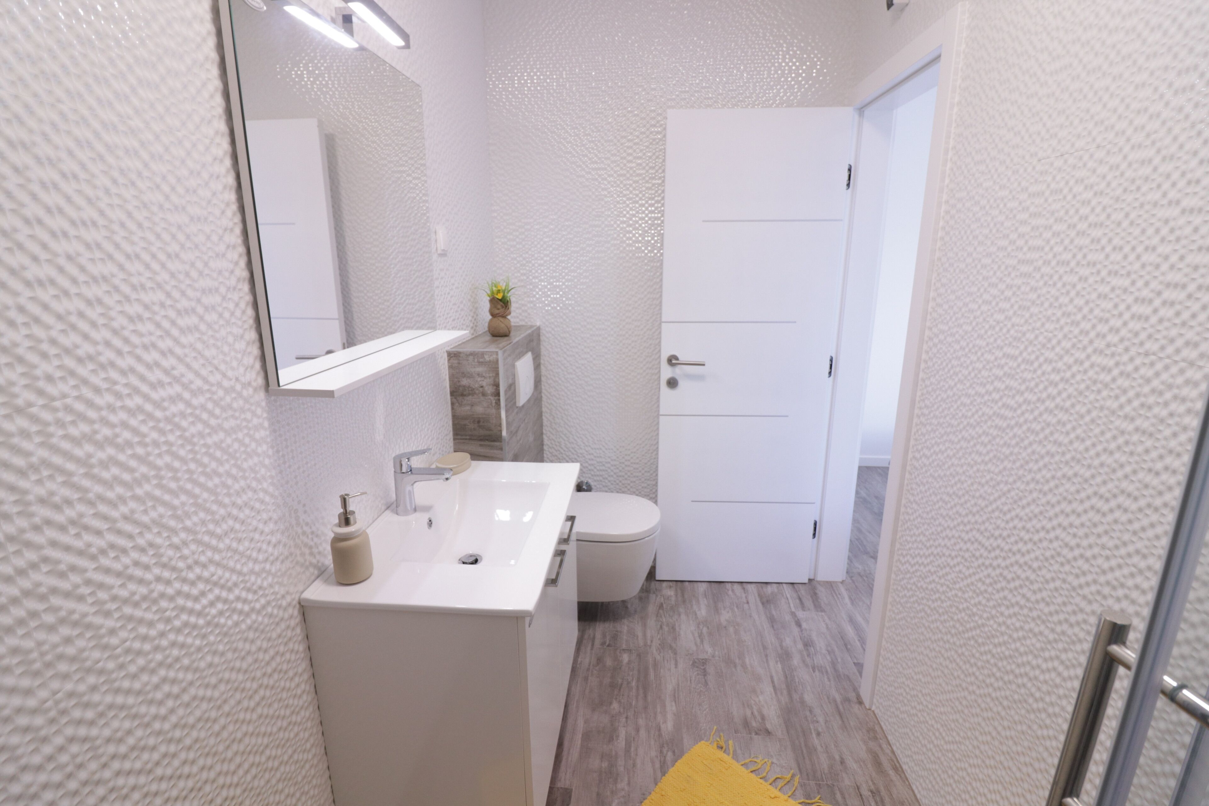 Et moderne badeværelse med hvid vask, spejl og toilet.