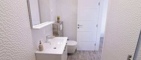 Et moderne badeværelse med hvid vask, spejl og toilet.