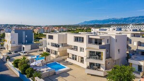 A modern apartment complex with a rooftop pool, multiple balconies, and a view of distant mountains. - Apartments & Rooms Danivan Pool Villas B (Novalja)